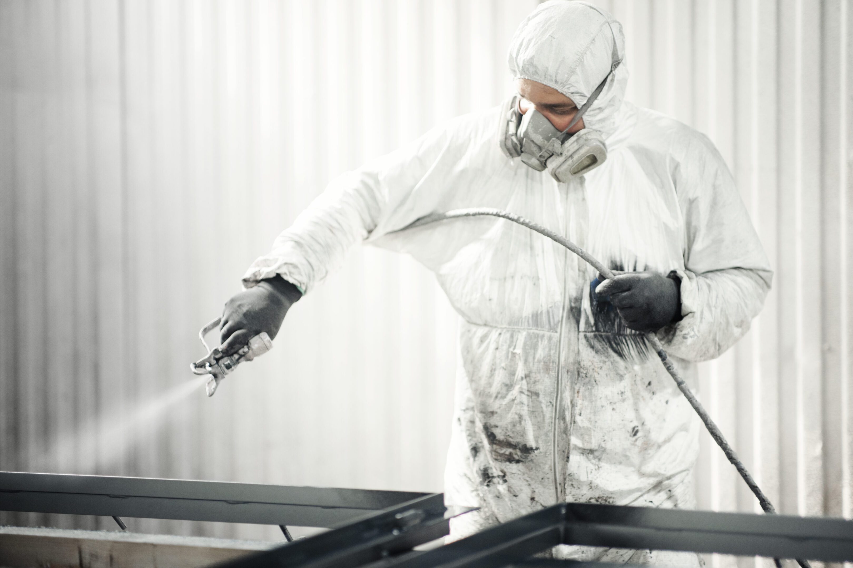 Closeup of an early 30's male using a compressor for spray painting steel plates at a factory facility.